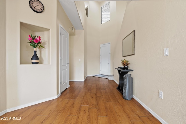 hallway featuring a high ceiling, light wood-type flooring, and baseboards