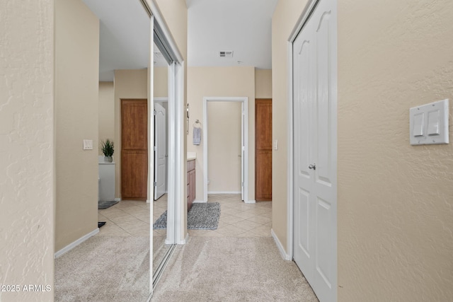 hall featuring visible vents, light colored carpet, light tile patterned flooring, and a textured wall