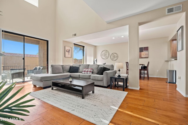 living room with a high ceiling, light wood-style floors, visible vents, and baseboards