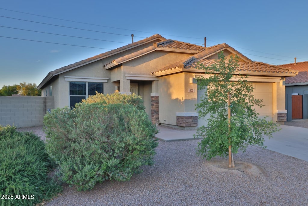 view of front of home featuring an attached garage, a tile roof, fence, and stucco siding