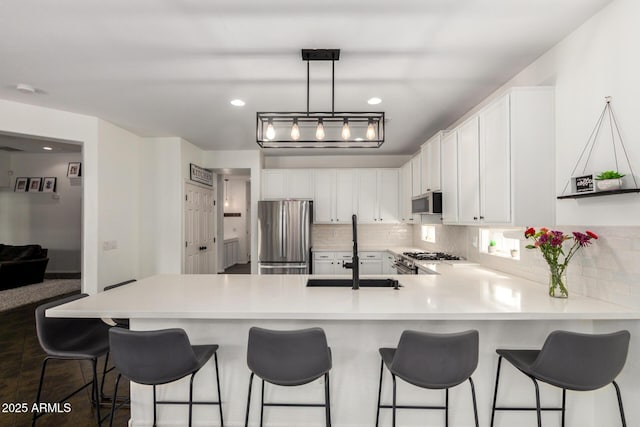 kitchen with decorative backsplash, a peninsula, white cabinets, a sink, and stainless steel appliances