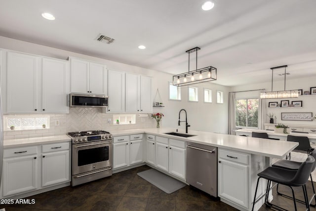 kitchen with appliances with stainless steel finishes, a sink, a peninsula, tasteful backsplash, and visible vents