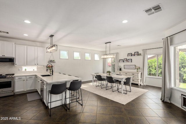 kitchen with visible vents, a peninsula, recessed lighting, a sink, and appliances with stainless steel finishes