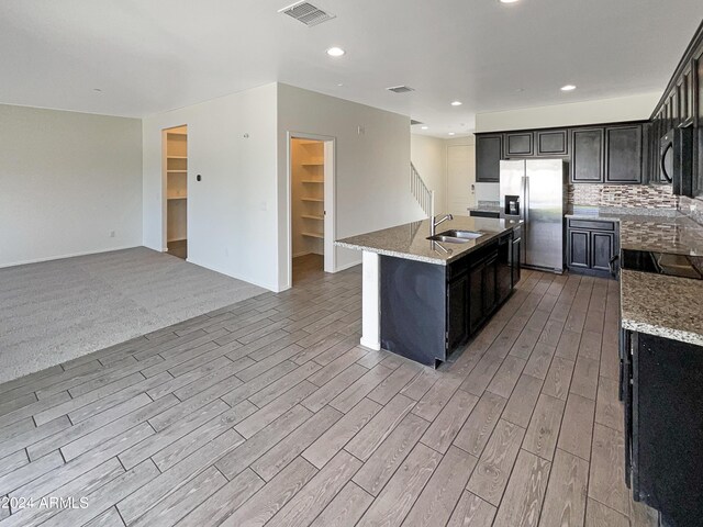 kitchen with backsplash, sink, appliances with stainless steel finishes, light hardwood / wood-style flooring, and a center island with sink