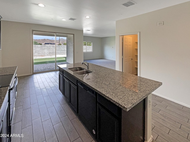 kitchen featuring black dishwasher, visible vents, light wood-style flooring, a kitchen island with sink, and a sink