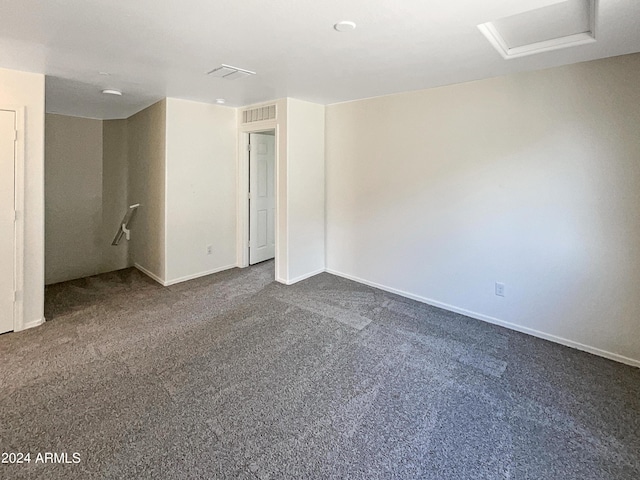 spare room with attic access, visible vents, dark carpet, and baseboards