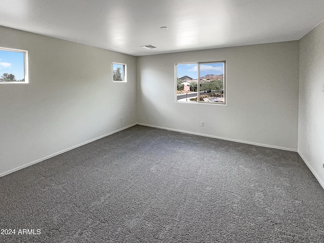 spare room with dark carpet, visible vents, plenty of natural light, and baseboards