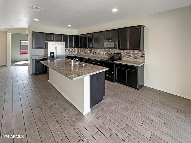 kitchen with backsplash, an island with sink, light stone counters, sink, and black appliances