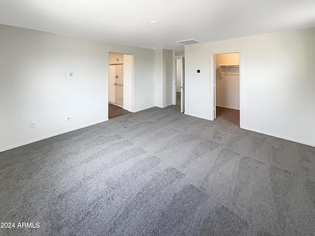 unfurnished bedroom with visible vents, a spacious closet, dark carpet, and baseboards