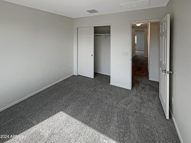 unfurnished bedroom featuring visible vents, baseboards, dark colored carpet, and a closet