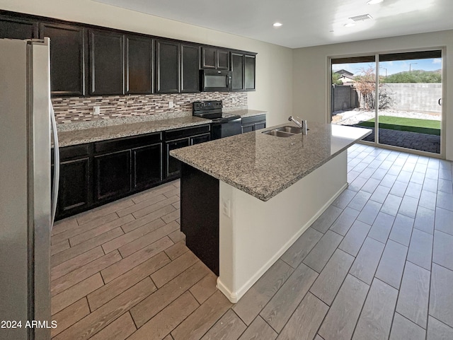 kitchen with backsplash, light stone counters, a kitchen island with sink, stove, and refrigerator