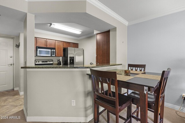 kitchen featuring appliances with stainless steel finishes, kitchen peninsula, light tile patterned floors, dark stone counters, and ornamental molding