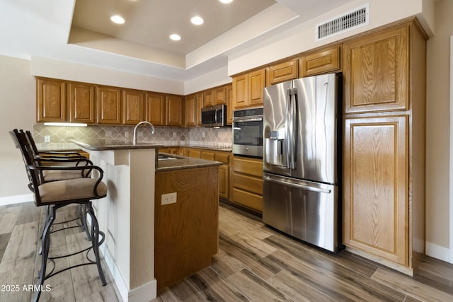 kitchen featuring dark hardwood / wood-style flooring, a raised ceiling, backsplash, a breakfast bar area, and stainless steel appliances