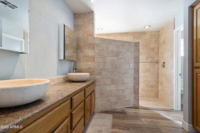 bathroom with wood-type flooring, tiled shower, toilet, and vanity