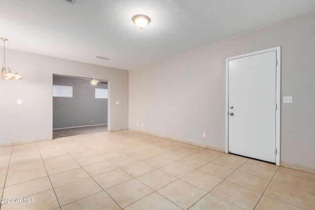 tiled empty room with ceiling fan with notable chandelier