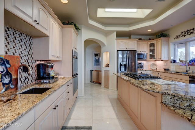 kitchen featuring a tray ceiling, arched walkways, stainless steel appliances, and a sink