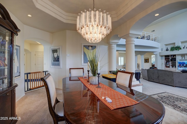 dining room featuring ornate columns, arched walkways, light carpet, a raised ceiling, and a notable chandelier