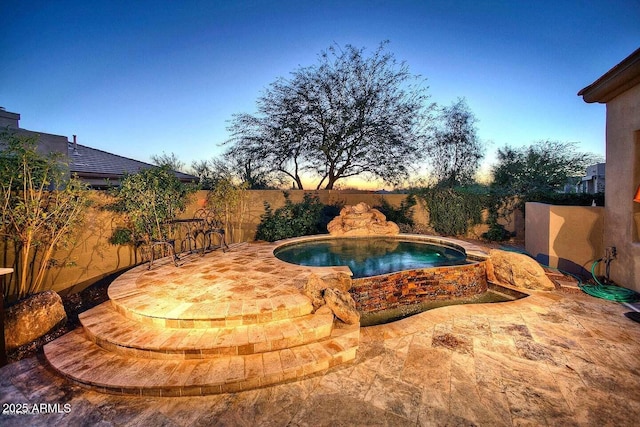 pool at dusk with an outdoor hot tub and a patio