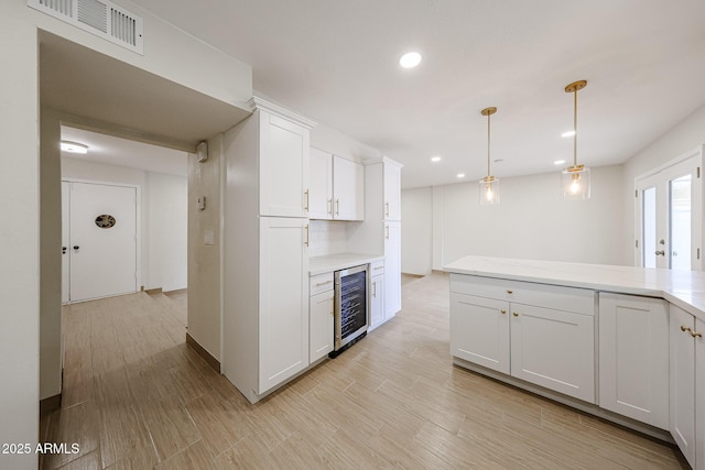 kitchen with wine cooler, white cabinetry, visible vents, light wood-style floors, and light countertops