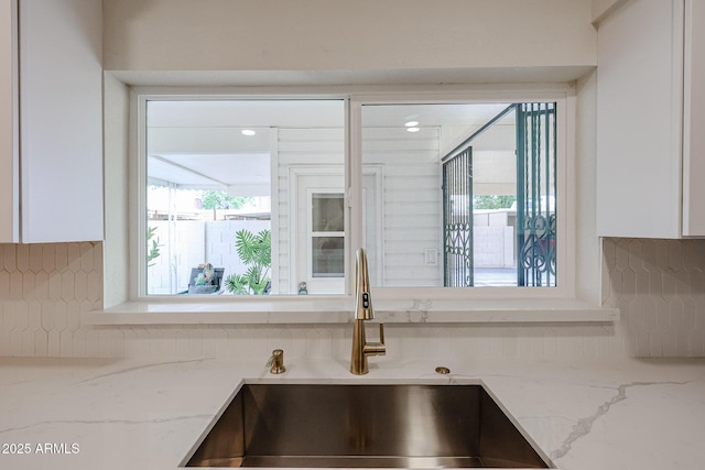 kitchen with light stone counters, plenty of natural light, white cabinets, and a sink