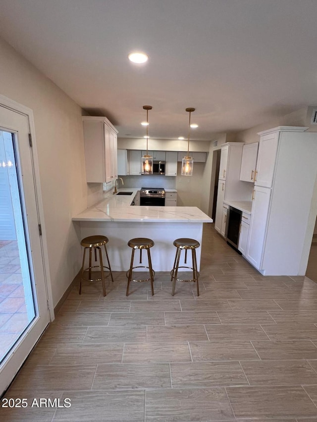 kitchen with a breakfast bar area, a peninsula, wood finish floors, a sink, and appliances with stainless steel finishes