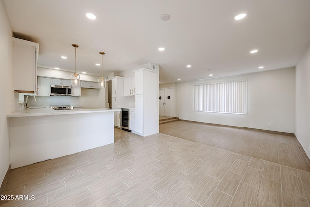 kitchen featuring light countertops, appliances with stainless steel finishes, open floor plan, a sink, and beverage cooler