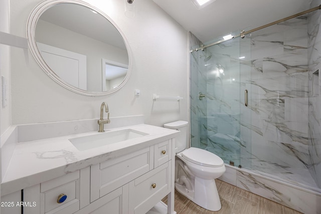 bathroom with toilet, a marble finish shower, wood finished floors, and vanity