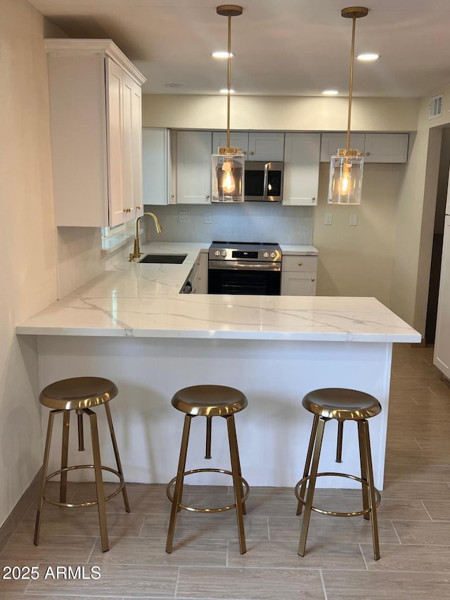 kitchen featuring stainless steel appliances, a peninsula, a sink, visible vents, and decorative backsplash