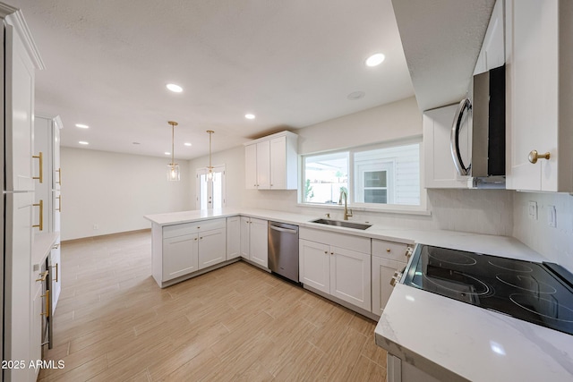 kitchen with light wood-style flooring, appliances with stainless steel finishes, a peninsula, light countertops, and a sink