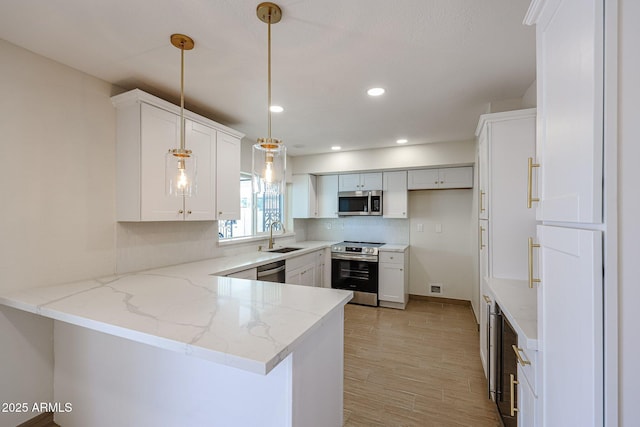 kitchen featuring appliances with stainless steel finishes, light stone counters, decorative light fixtures, a peninsula, and a sink