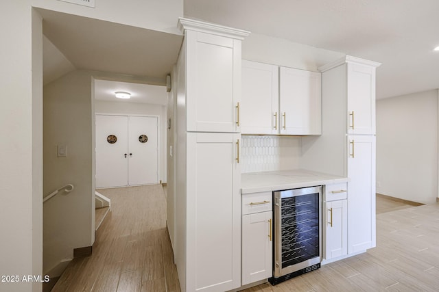 bar with beverage cooler, a bar, baseboards, and light wood-style floors