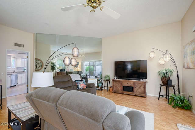 living room featuring visible vents, baseboards, a textured ceiling, and ceiling fan