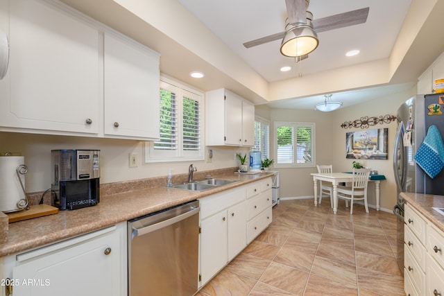 kitchen featuring a ceiling fan, a sink, stainless steel appliances, white cabinets, and a raised ceiling