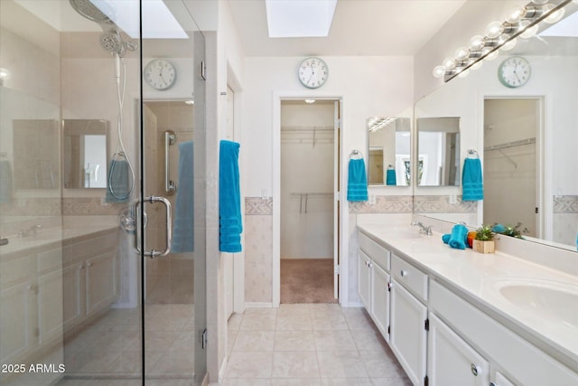 full bathroom featuring double vanity, a stall shower, a skylight, and a sink