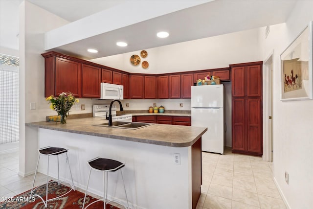 kitchen with a peninsula, white appliances, dark brown cabinets, and a sink