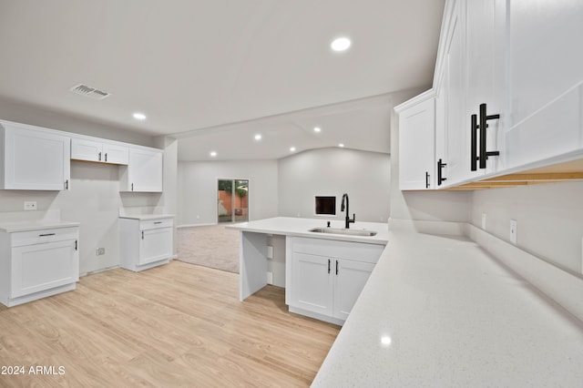 kitchen with lofted ceiling, sink, light wood-type flooring, and white cabinetry