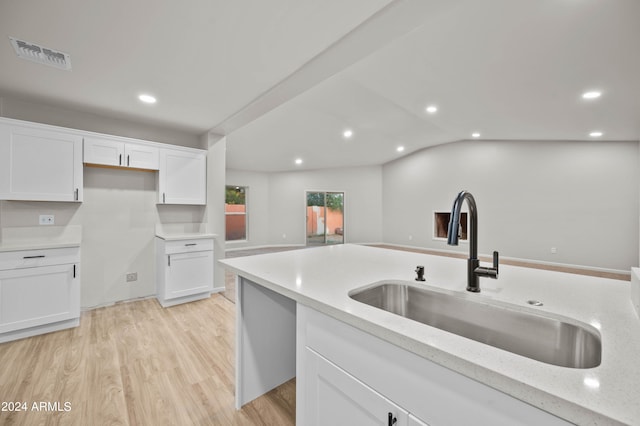 kitchen featuring white cabinets, light stone counters, light hardwood / wood-style floors, sink, and lofted ceiling