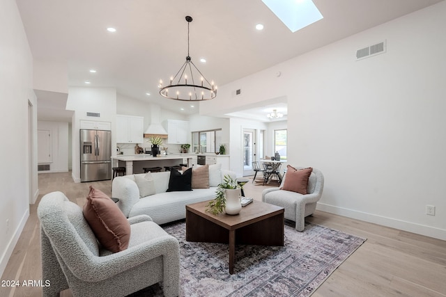 living room with light hardwood / wood-style floors, high vaulted ceiling, a skylight, and a notable chandelier