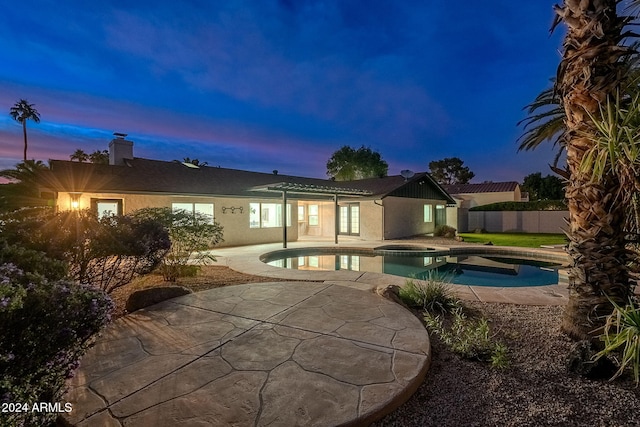 pool at dusk featuring an in ground hot tub and a patio