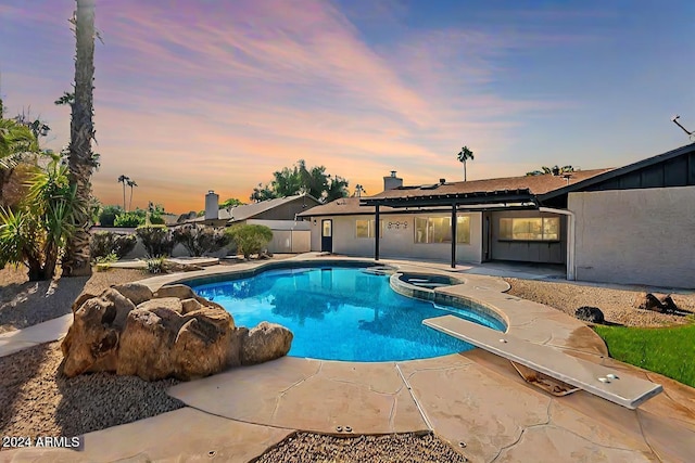 pool at dusk featuring a patio area, an in ground hot tub, and a diving board