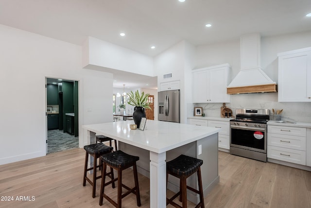 kitchen with white cabinets, custom range hood, stainless steel appliances, and light hardwood / wood-style flooring