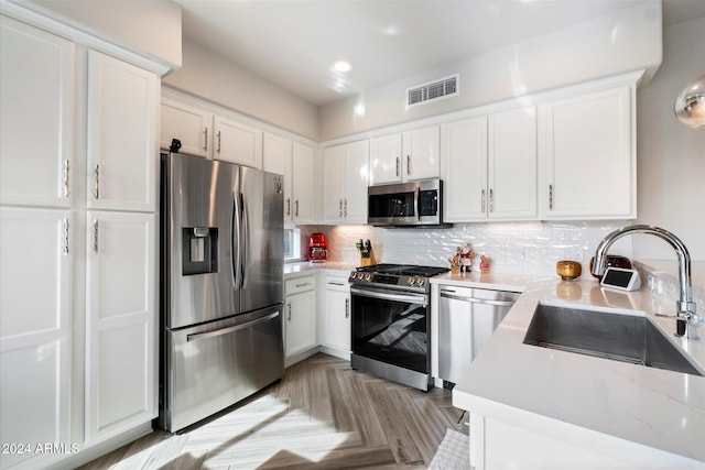 kitchen featuring light stone countertops, stainless steel appliances, light parquet floors, sink, and white cabinets