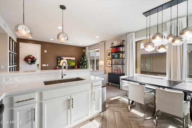 kitchen featuring light parquet floors, decorative light fixtures, white cabinetry, and sink