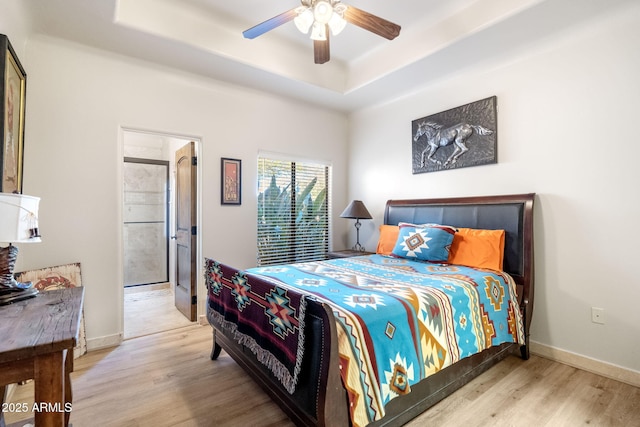 bedroom featuring connected bathroom, a tray ceiling, light hardwood / wood-style flooring, and ceiling fan