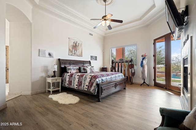 bedroom with a raised ceiling, light wood-type flooring, access to outside, and ceiling fan