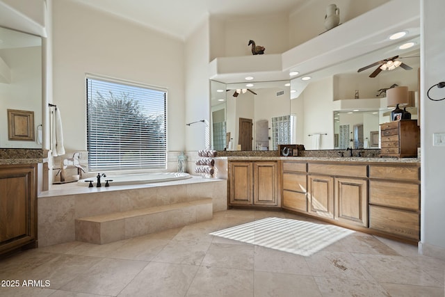 bathroom featuring tiled tub, vanity, a towering ceiling, ceiling fan, and tile patterned flooring