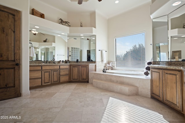 bathroom featuring vanity, a relaxing tiled tub, ceiling fan, and a high ceiling