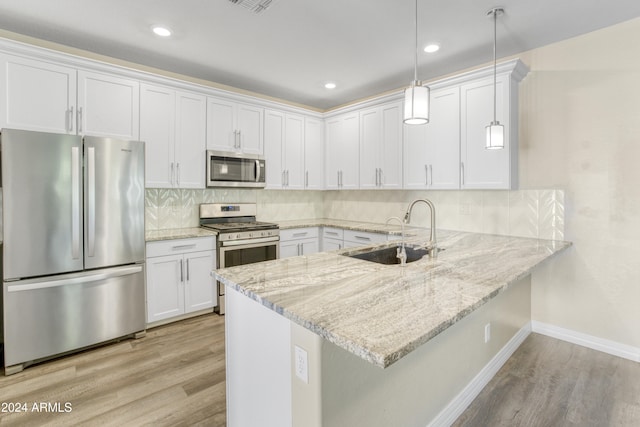 kitchen featuring stainless steel appliances, a sink, light wood-style flooring, a peninsula, and baseboards