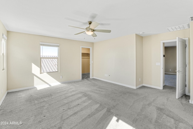 unfurnished bedroom featuring carpet floors, baseboards, a walk in closet, and a ceiling fan