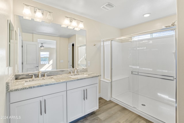 bathroom featuring wood finished floors, a shower stall, double vanity, and ceiling fan